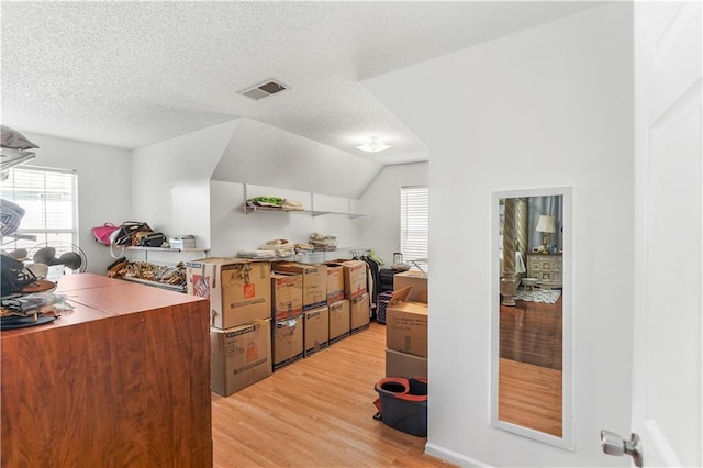 kitchen with light wood-type flooring, visible vents, a textured ceiling, and vaulted ceiling