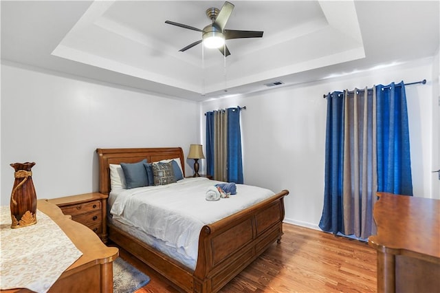 bedroom featuring visible vents, a ceiling fan, a tray ceiling, and wood finished floors