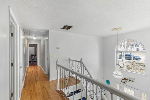 hall with visible vents, an upstairs landing, a textured ceiling, light wood-style floors, and attic access