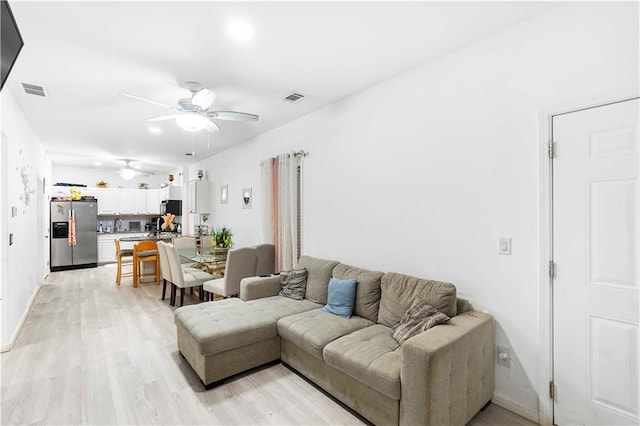 living area featuring visible vents, baseboards, a ceiling fan, and light wood finished floors