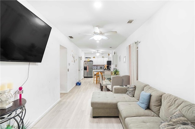 living room with light wood finished floors, visible vents, baseboards, and ceiling fan