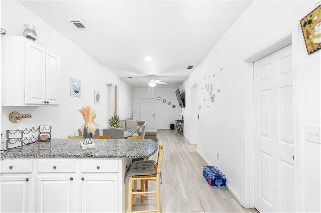 kitchen featuring a breakfast bar area, visible vents, a peninsula, ceiling fan, and white cabinetry