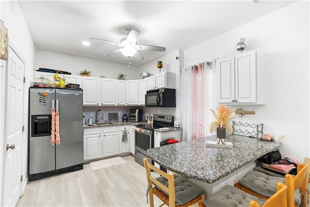 kitchen with a kitchen bar, light wood-style flooring, a sink, appliances with stainless steel finishes, and a peninsula