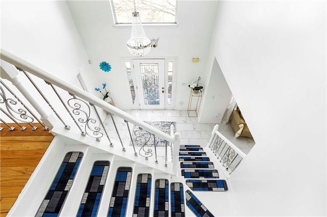 stairway with a chandelier, marble finish floor, and a towering ceiling