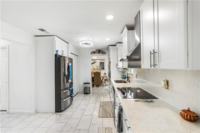 kitchen with visible vents, white cabinets, marble finish floor, black electric stovetop, and stainless steel fridge