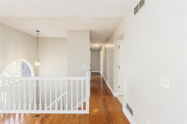 hall with wood finished floors, visible vents, and baseboards