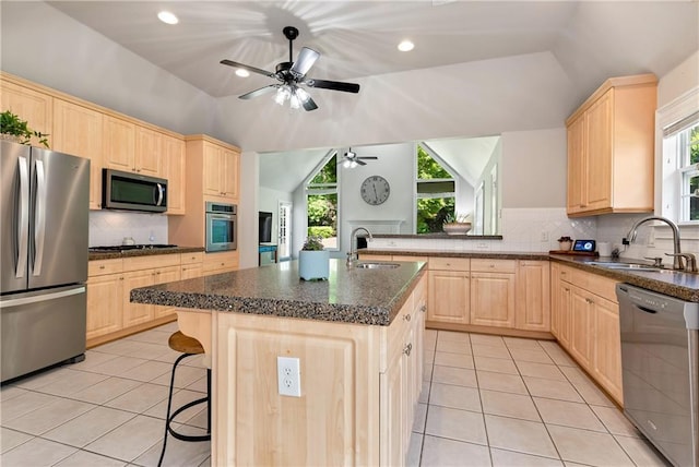 kitchen with stainless steel appliances, light brown cabinets, a sink, light tile patterned floors, and vaulted ceiling