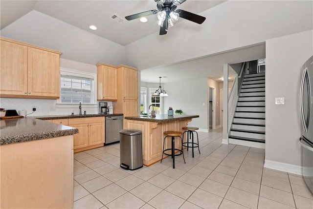 kitchen with light brown cabinetry, stainless steel appliances, lofted ceiling, a breakfast bar, and light tile patterned floors