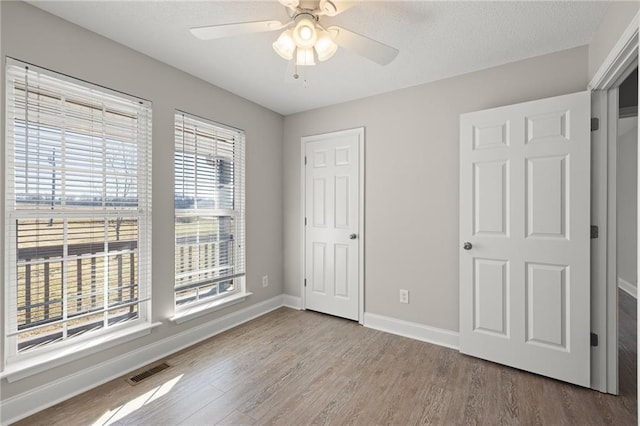 unfurnished bedroom with visible vents, a textured ceiling, baseboards, and wood finished floors