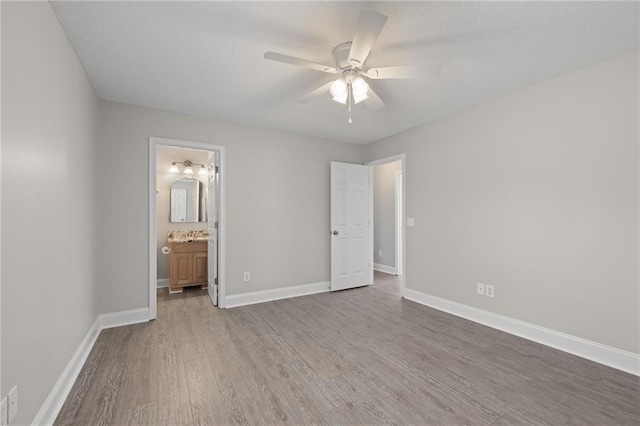 unfurnished bedroom with a ceiling fan, a textured ceiling, wood finished floors, connected bathroom, and baseboards