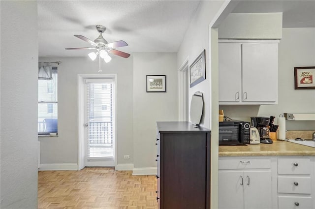 kitchen with light parquet floors, a textured ceiling, white cabinets, and ceiling fan