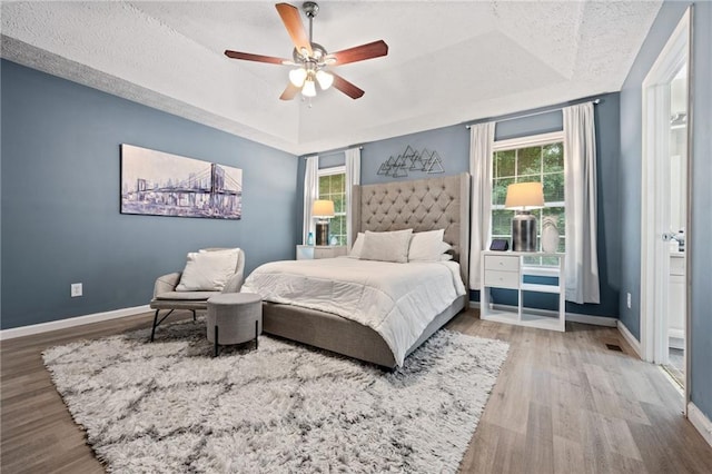 bedroom with a tray ceiling, multiple windows, and wood finished floors