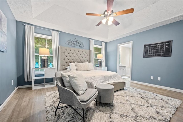 bedroom with baseboards, multiple windows, a raised ceiling, and wood finished floors