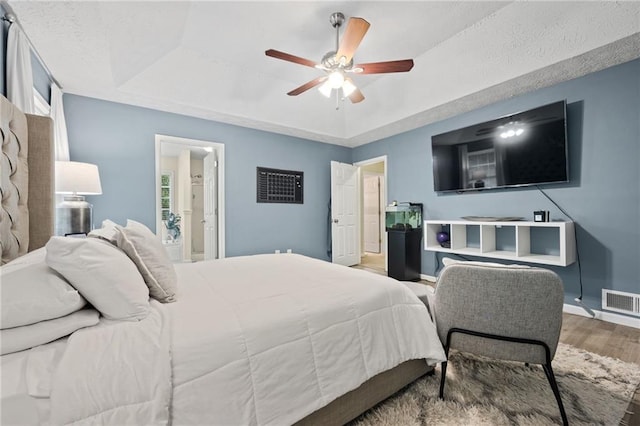 bedroom featuring baseboards, visible vents, wood finished floors, and a raised ceiling