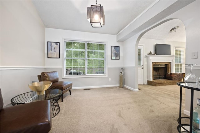 living area with carpet flooring, a brick fireplace, visible vents, and arched walkways
