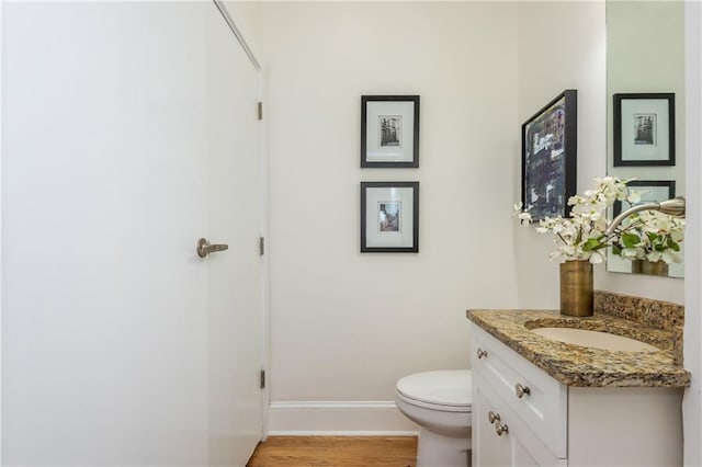 half bathroom featuring vanity, baseboards, toilet, and wood finished floors