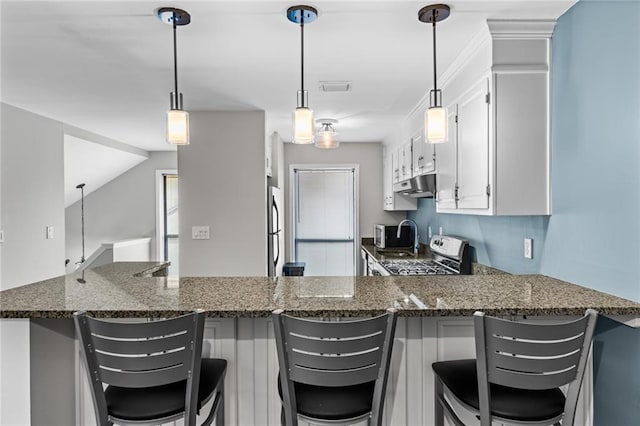 kitchen featuring range with gas cooktop, freestanding refrigerator, dark stone countertops, a peninsula, and under cabinet range hood