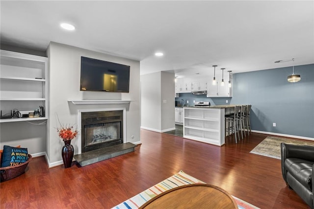 living room with wet bar, baseboards, wood finished floors, and a glass covered fireplace