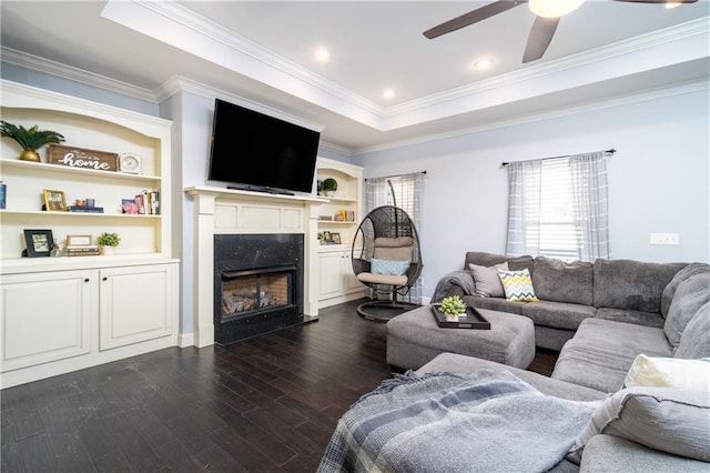 living room featuring a high end fireplace, a tray ceiling, crown molding, dark wood-type flooring, and built in shelves