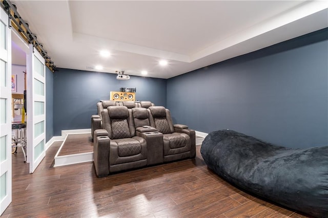 home theater room featuring a barn door, dark wood-type flooring, and a tray ceiling