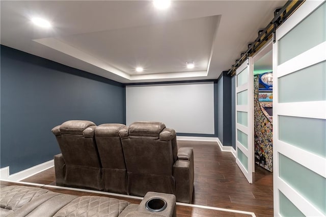 home theater featuring dark hardwood / wood-style floors, a tray ceiling, and a barn door