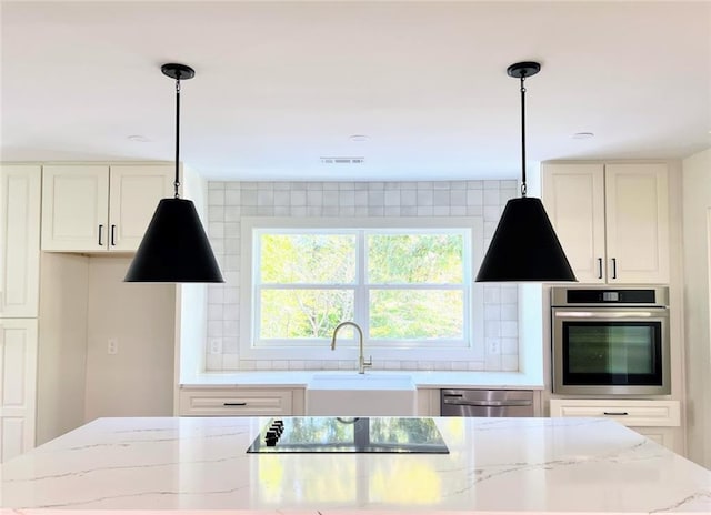 kitchen with sink, light stone counters, tasteful backsplash, hanging light fixtures, and appliances with stainless steel finishes