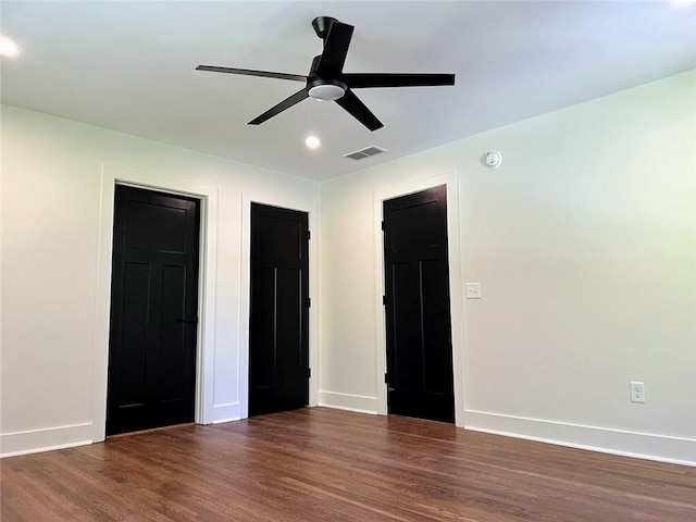 unfurnished bedroom with multiple closets, ceiling fan, and dark hardwood / wood-style flooring