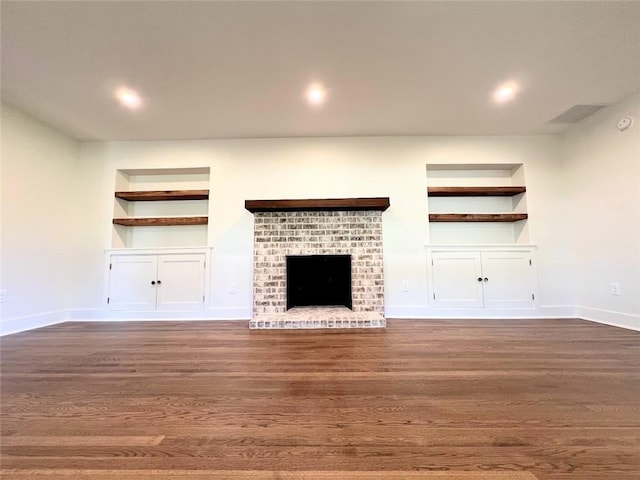 unfurnished living room featuring a fireplace, dark hardwood / wood-style flooring, and built in shelves