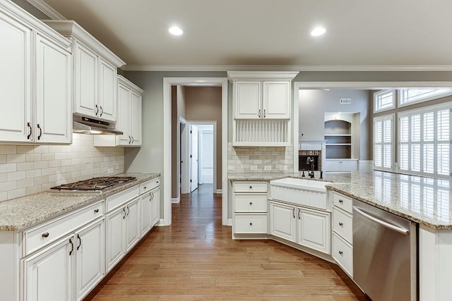 kitchen featuring light wood finished floors, a sink, stainless steel appliances, under cabinet range hood, and crown molding