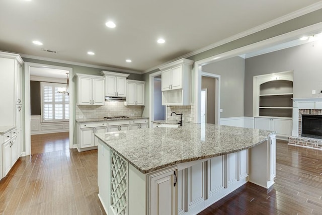 kitchen featuring crown molding, stainless steel gas cooktop, under cabinet range hood, light stone counters, and wood finished floors