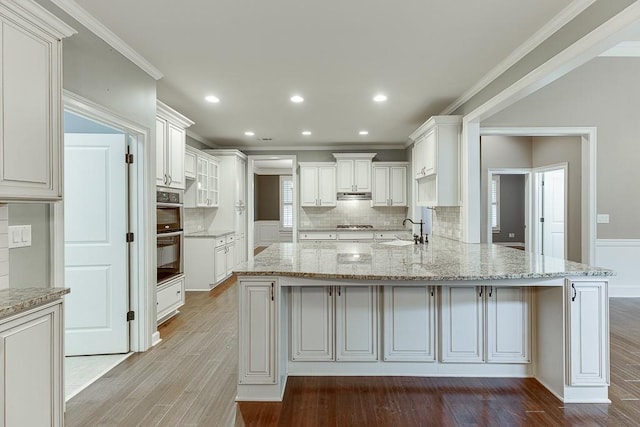 kitchen with light stone counters, a peninsula, wood finished floors, and ornamental molding