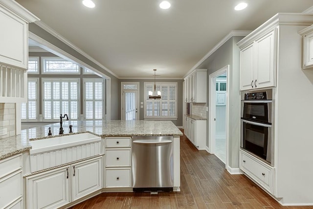 kitchen with dark wood-type flooring, a chandelier, ornamental molding, stainless steel appliances, and a sink