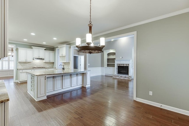 kitchen with a notable chandelier, under cabinet range hood, dark wood-style floors, white cabinets, and decorative backsplash