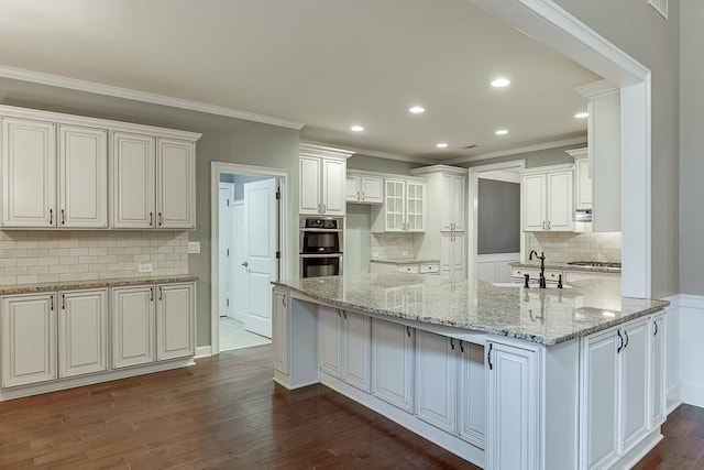 kitchen with ornamental molding, light stone countertops, dark wood-style flooring, and a sink