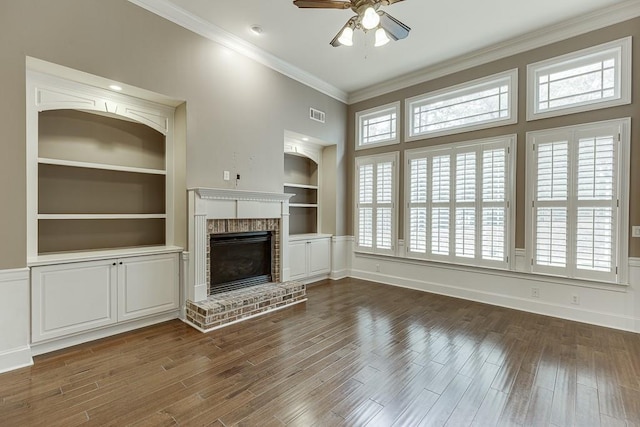 unfurnished living room featuring built in shelves, dark wood-style floors, a fireplace, ceiling fan, and crown molding