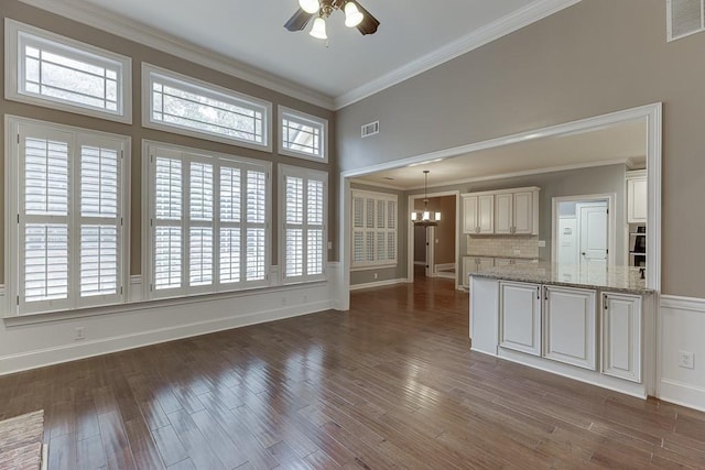 unfurnished living room with crown molding, ceiling fan with notable chandelier, dark wood-type flooring, and visible vents