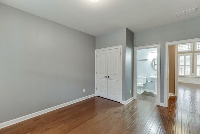 unfurnished bedroom featuring visible vents, baseboards, wood finished floors, a closet, and ensuite bath