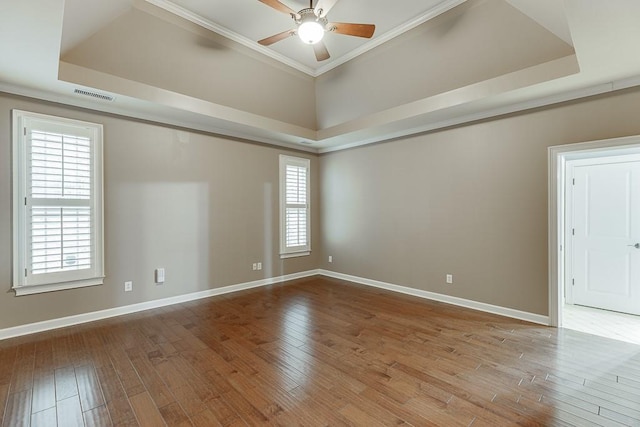 unfurnished room featuring hardwood / wood-style floors, baseboards, visible vents, a tray ceiling, and ceiling fan