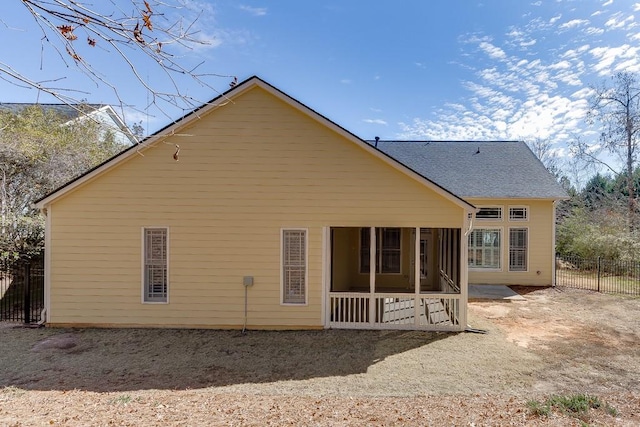 back of house with a sunroom, roof with shingles, and fence