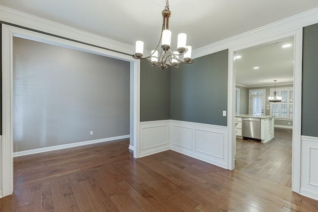 spare room with ornamental molding, dark wood-style floors, wainscoting, a decorative wall, and a chandelier