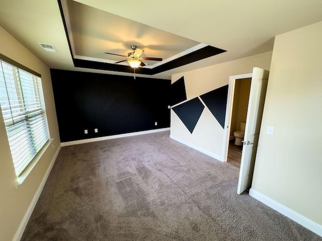 carpeted spare room featuring ceiling fan, a raised ceiling, visible vents, and baseboards