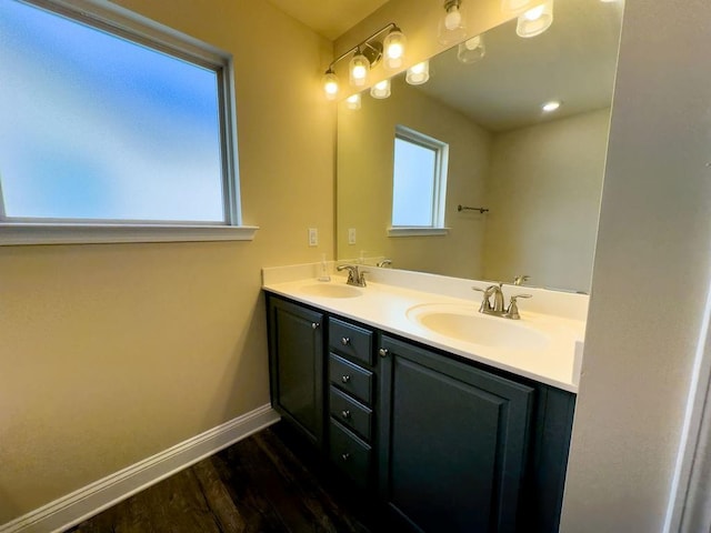 bathroom with double vanity, baseboards, a sink, and wood finished floors