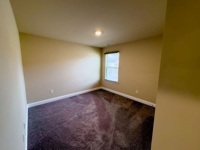 unfurnished room with dark carpet, visible vents, and baseboards