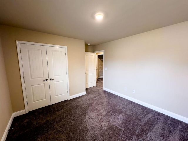 unfurnished bedroom with a closet, dark carpet, and baseboards