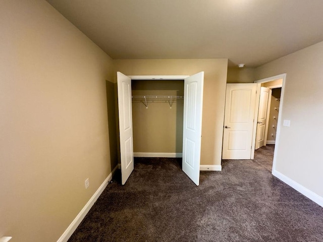 unfurnished bedroom featuring a closet, dark carpet, and baseboards