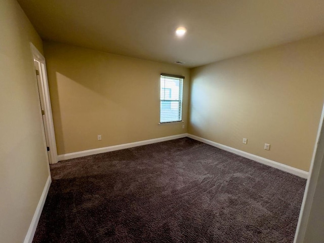 spare room featuring dark colored carpet, visible vents, and baseboards