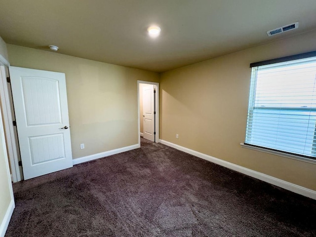 unfurnished room with visible vents, dark carpet, and baseboards