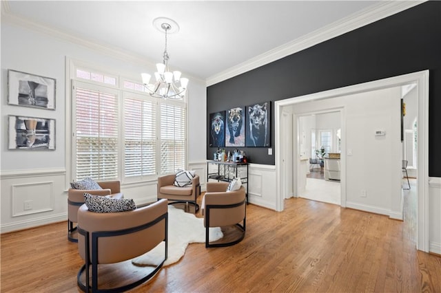 living area with ornamental molding, plenty of natural light, light wood-style floors, a chandelier, and a wainscoted wall