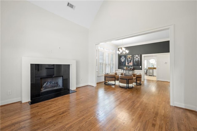living area featuring a chandelier, wood finished floors, baseboards, high vaulted ceiling, and a fireplace with raised hearth
