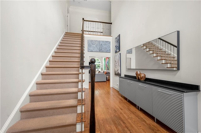 stairs with a high ceiling, wood finished floors, baseboards, and ornamental molding